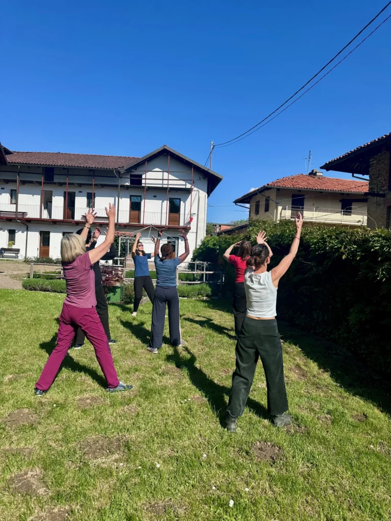 Quatre personnes font des étirements dans un jardin ensoleillé devant des maisons traditionnelles.